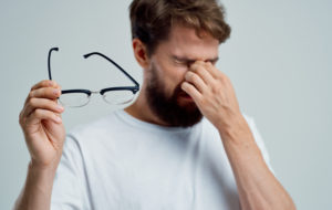 man taking off his glasses and rubbing his eyes due to dry eye symptoms