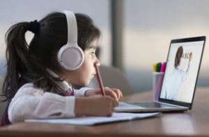 a young girl wearing headphones and holding a pencil stares into a computer screen