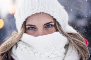 A young woman bundled up in the snow in a white hat and scarf