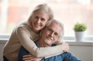 Smiling caring middle aged wife embracing senior husband at home