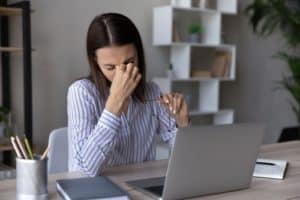 a woman sitting in front of a laptop a strained and uncomfortable expression on their face