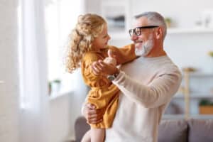 positive grandpa holding hands while dancing together in living room at home