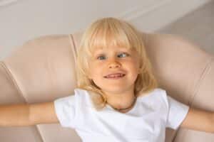Young child smiling on a chair. This kid has strabismus, better known as being cross eyed