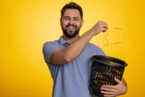 A man holding a trash can and dropping his glasses into it