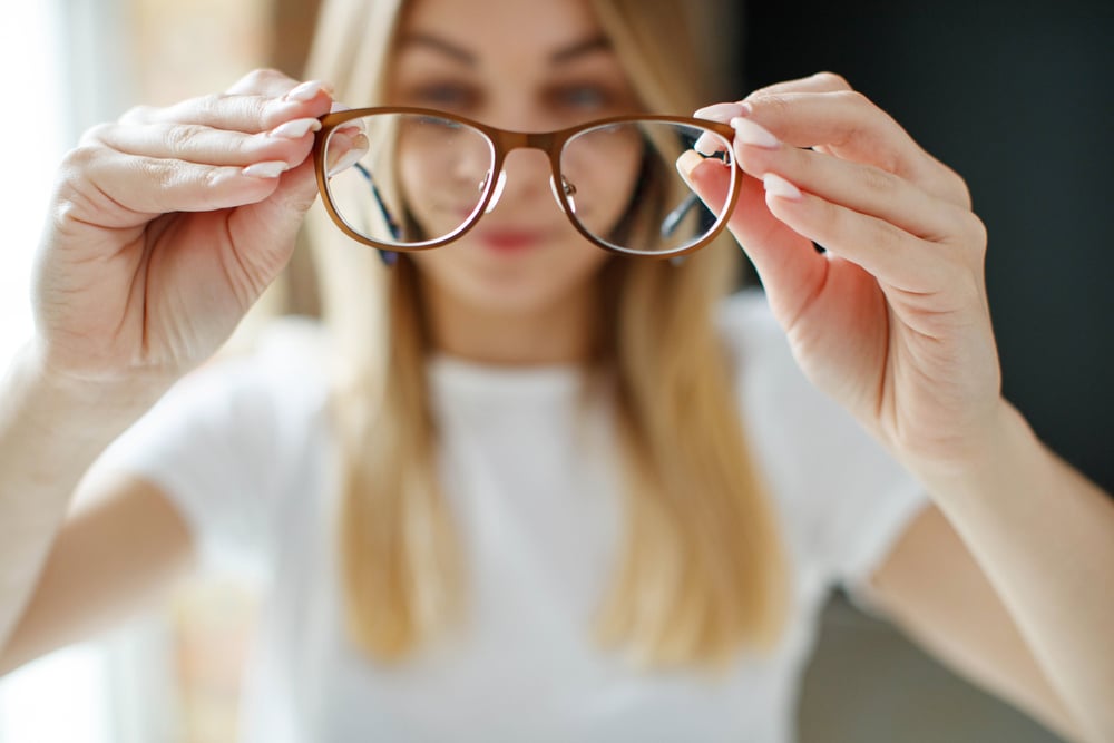 Woman holding out her eyeglasses in Loveland, CO.