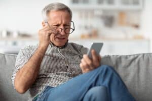 Man with glasses struggling to see his phone from age-related macular degeneration in Loveland