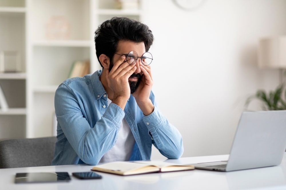 Man rubbing his eyes with color blindness while at the computer in Loveland, CO