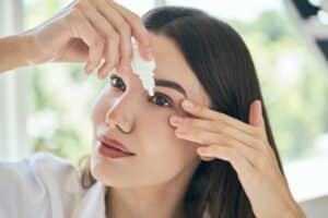 Woman putting medicated eye drops in her eye for thyroid eye disorder treatment in Loveland, CO
