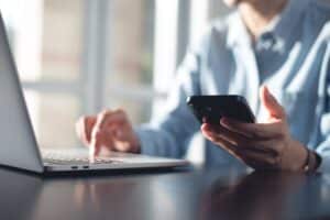 Person at computer holding phone that exacerbate dry eye symptoms in Loveland