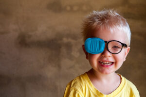 Young boy smiling wearing glasses and a patch over one eye due to strabismus in Loveland, CO