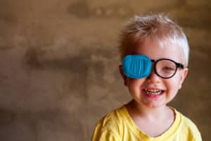 Young child smiling with glasses and eye patch after Strabismus surgery in Loveland, CO