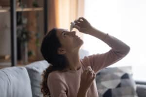 Woman putting eye drops in her eye to help with red eyes in Loveland, CO