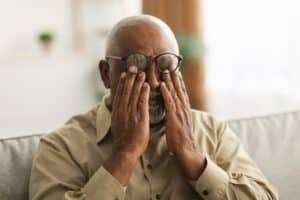Man with hands over eyes from thyroid eye disease in Loveland, CO